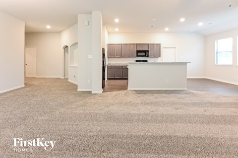 A spacious, well-lit kitchen and living room with a carpeted floor.