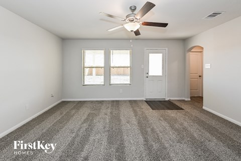 A spacious empty room with a carpeted floor and a ceiling fan.