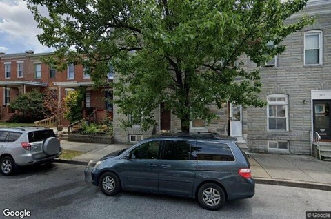A street view with a car and a tree in front of a building.