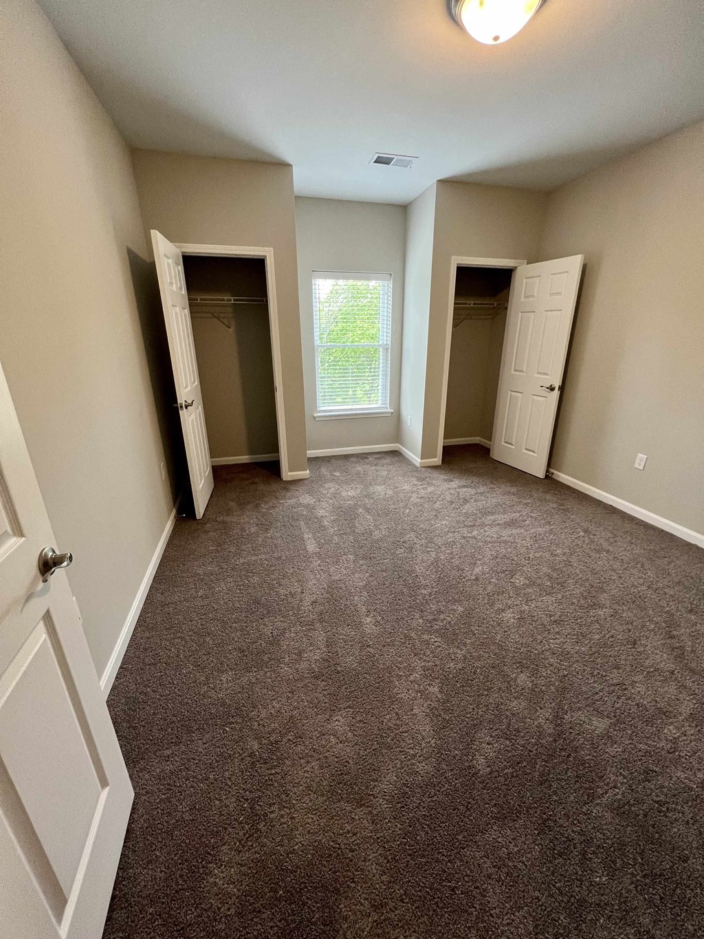 a carpeted room with two closets and a window
