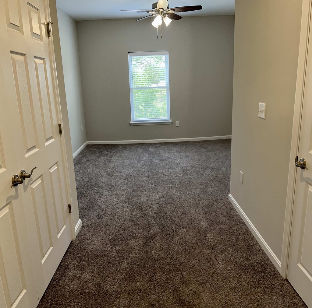 a carpeted room with a ceiling fan and a window