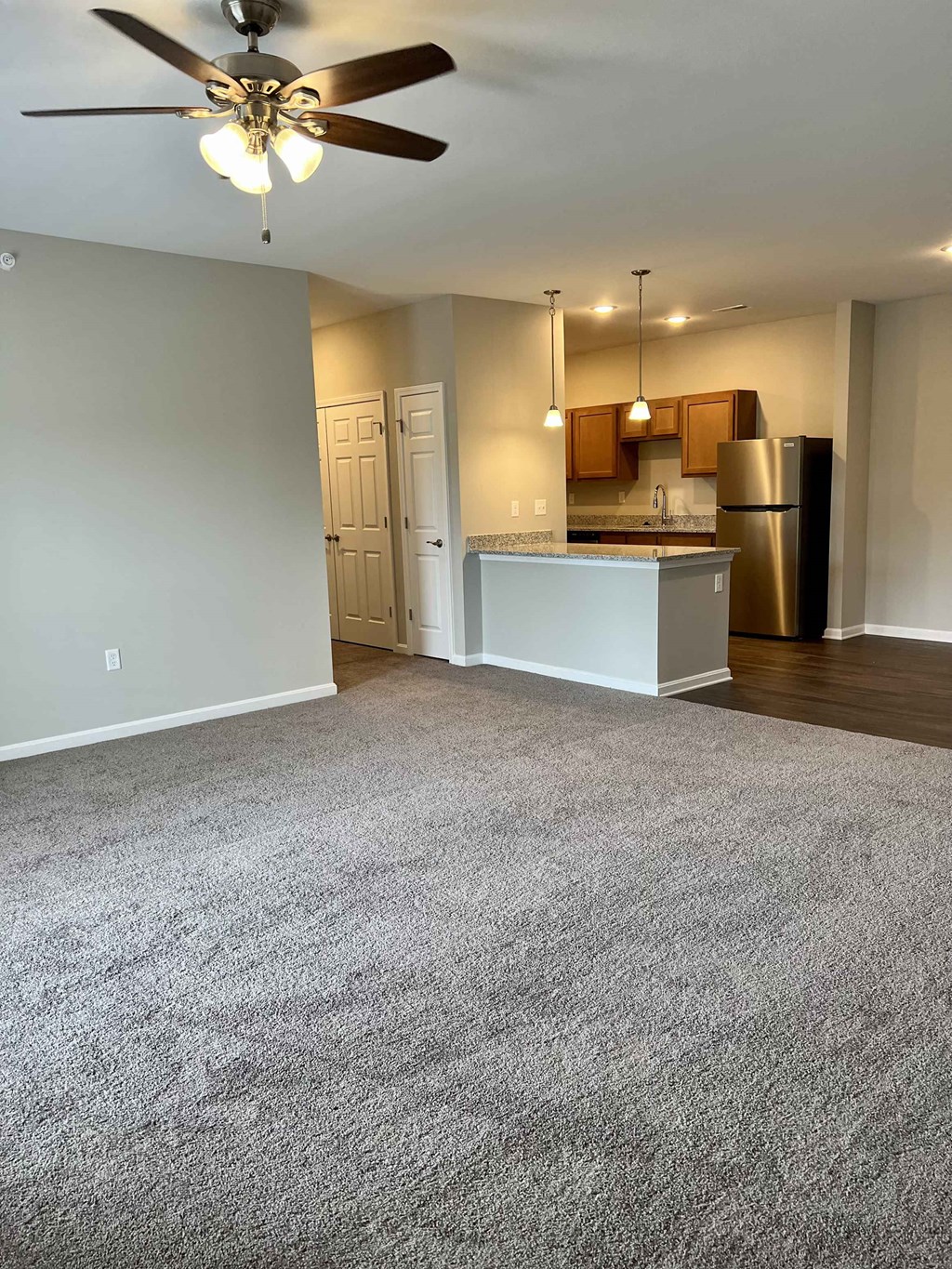an empty living room with a kitchen and a ceiling fan