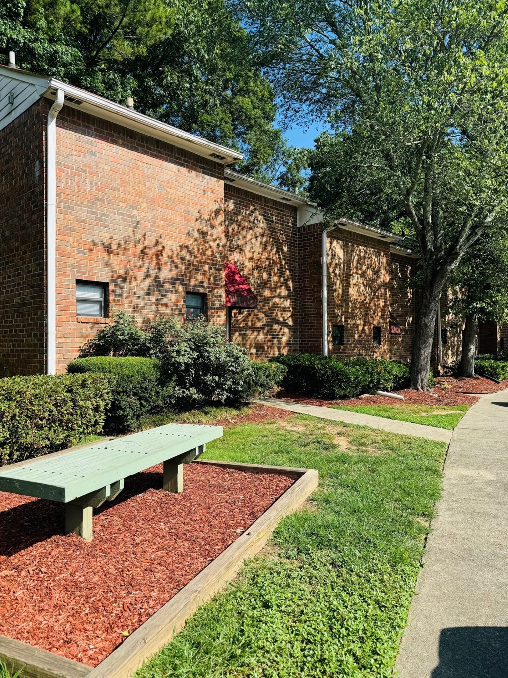 A red brick building with a green bench in front of it.