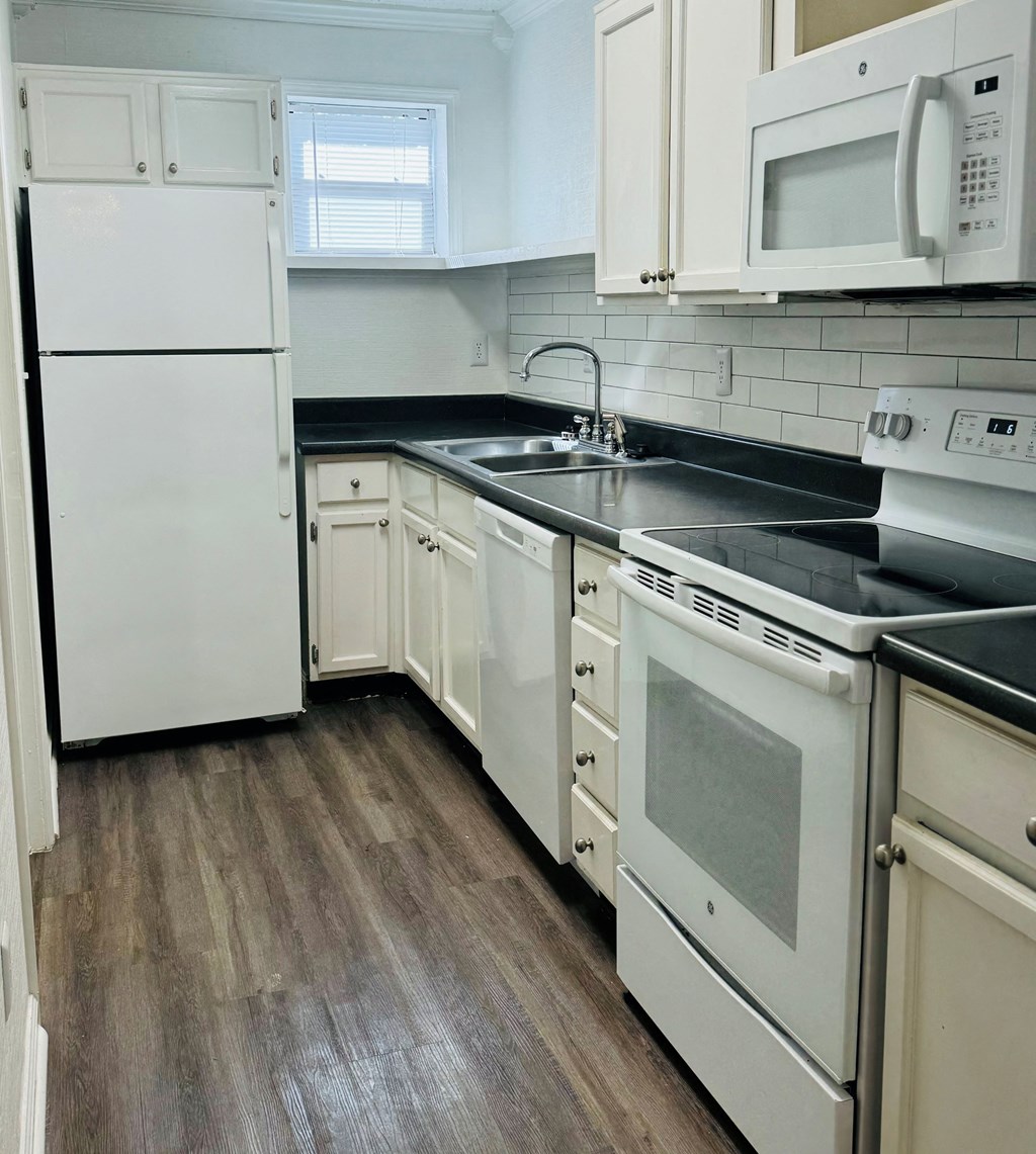 A kitchen with white appliances and wooden floors.