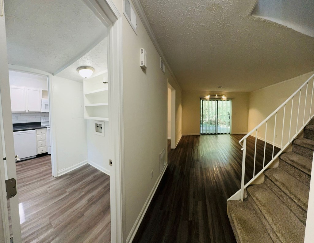 A hallway with a staircase on the right and a kitchen visible through the open door on the left.