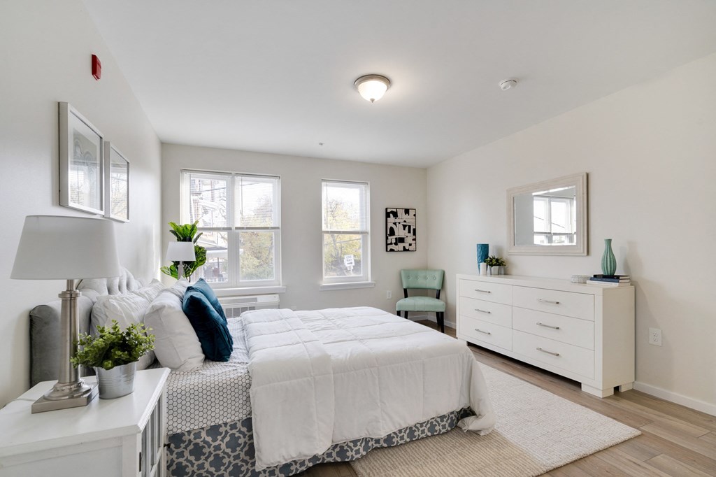 a bedroom with a bed and a dresser and two windows