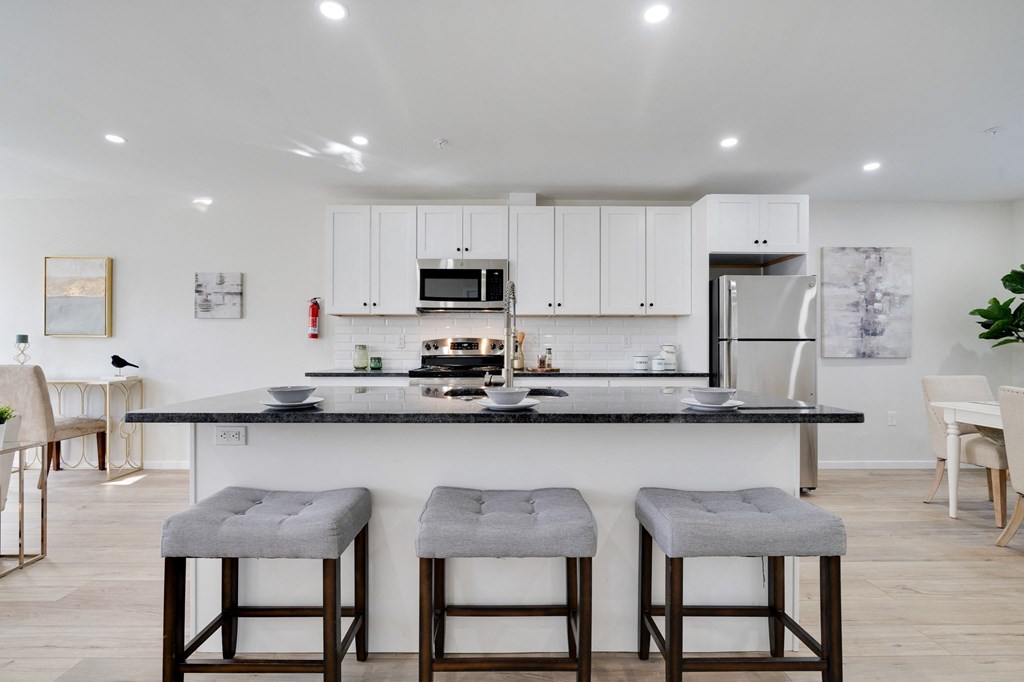 a kitchen with white cabinets and a counter with three stools