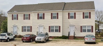 A white house with red trim and a grey car parked in front.