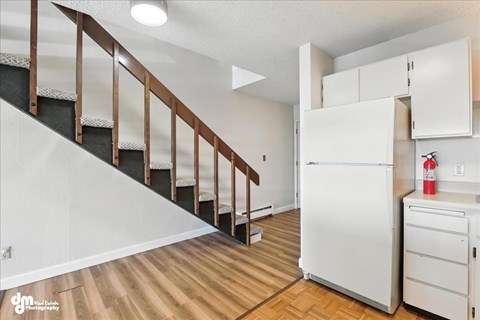 A white refrigerator in a kitchen with wooden floors and a staircase.