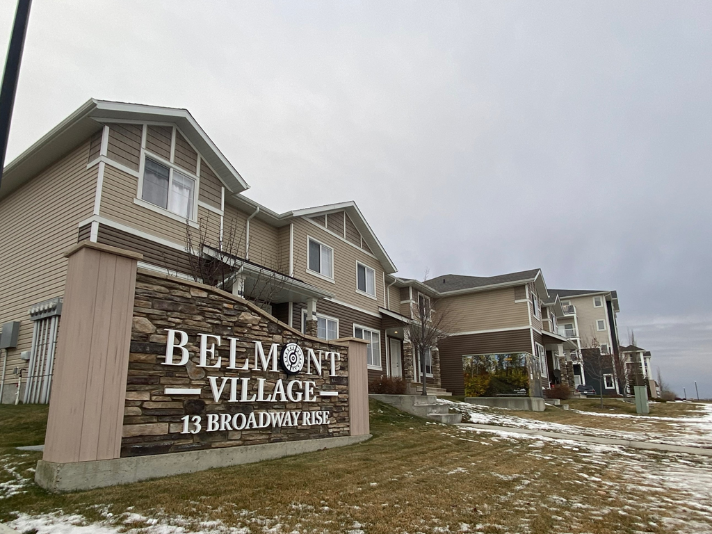 A sign in front of apartment buildings that says Belmont Village.