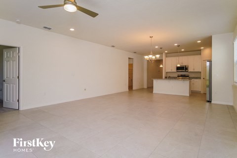 A spacious living room with a ceiling fan and a kitchen in the background.