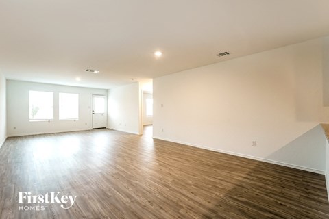 A spacious room with wooden flooring and white walls, with a window on the left side.
