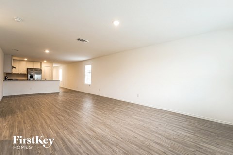 A spacious room with wooden flooring and a kitchen area in the background.