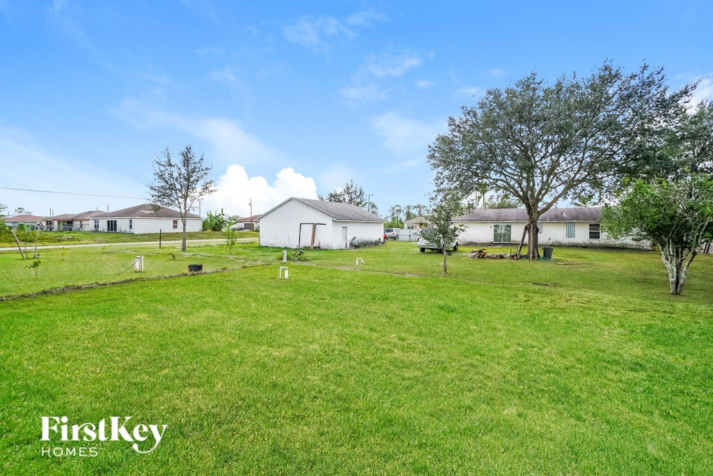 A grassy field with a white house and trees in the background.