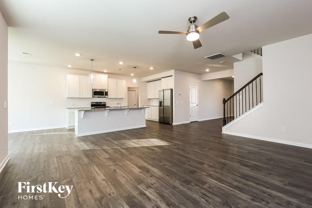 A spacious living room with a kitchen in the background and a staircase on the right.
