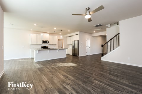 A spacious living room with a kitchen in the background and a staircase on the right.