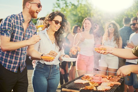 A group of people are gathered around a barbecue grill, enjoying a sunny day outdoors.