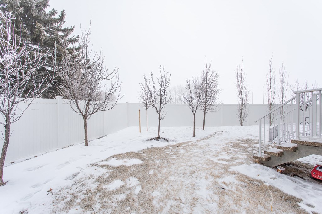 A snowy landscape with a red car and a white fence.