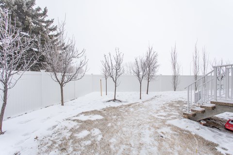 A snowy landscape with a red car and a white fence.