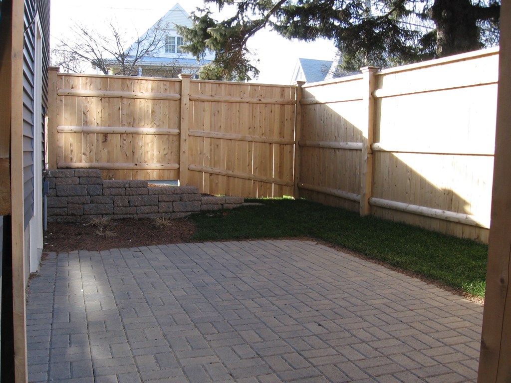 a backyard with a wooden fence and a brick driveway
