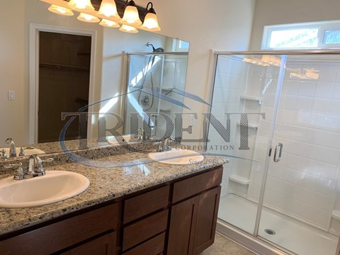 A bathroom with a double sink and a glass shower door.