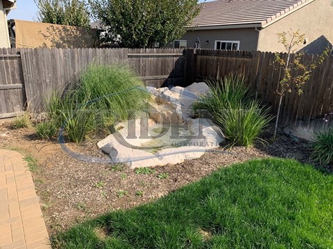 A garden with a fence and a small waterfall.