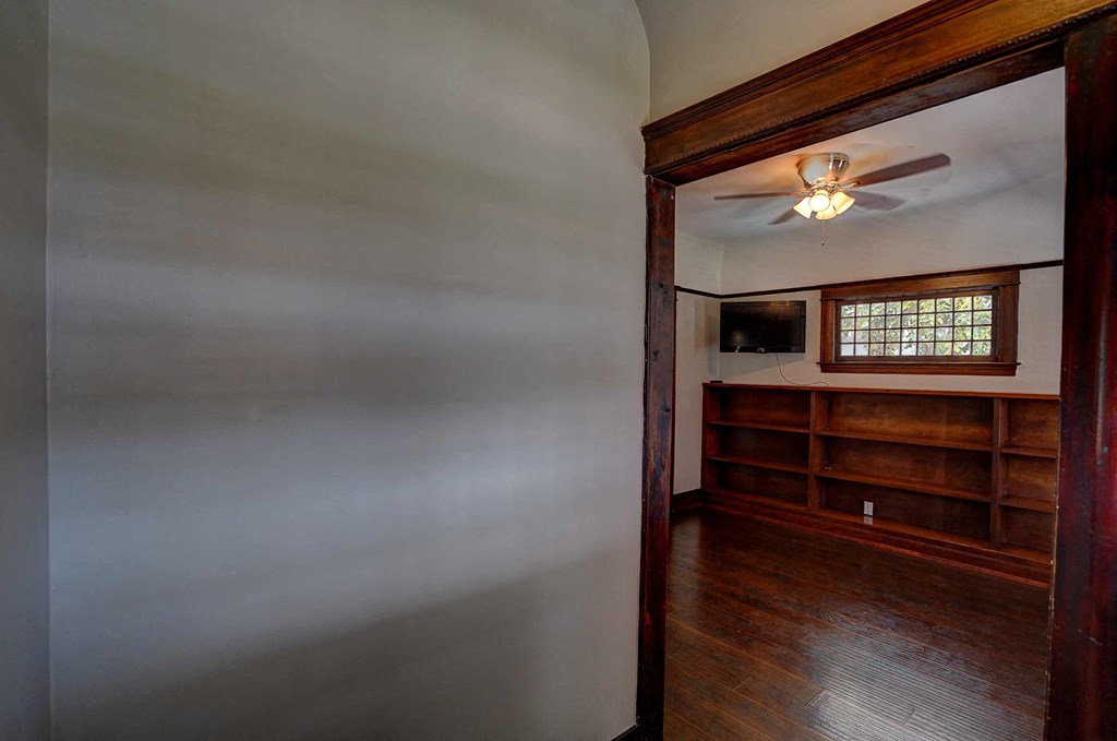 an empty living room with a ceiling fan and a book shelf