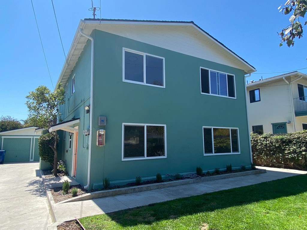 the exterior of a green house with a sidewalk and lawn