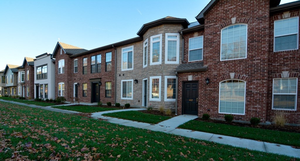 a row of brick houses with sidewalk and grass