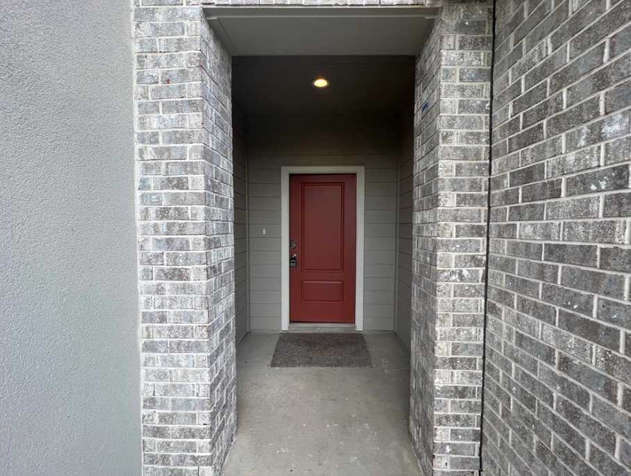 A red door is visible through a gap in a grey brick wall.