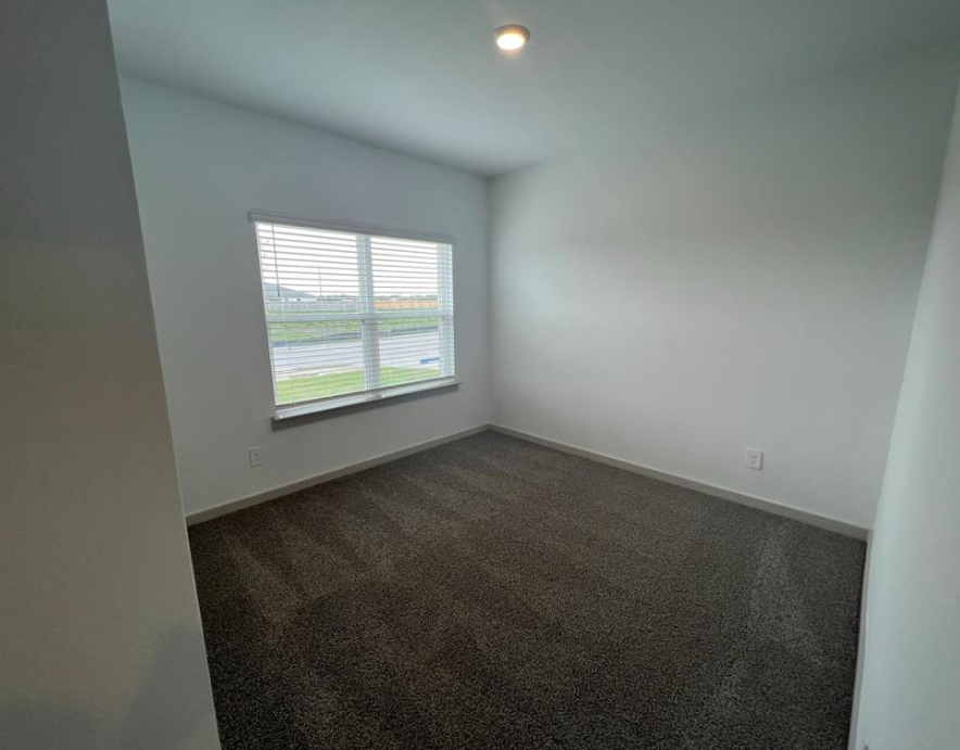 A room with a carpeted floor and a window with blinds.