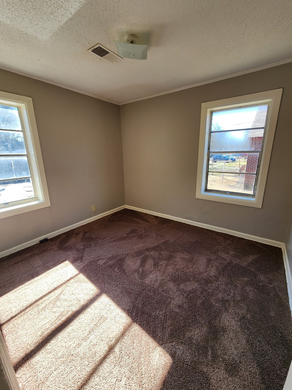 an empty room with carpet and two windows