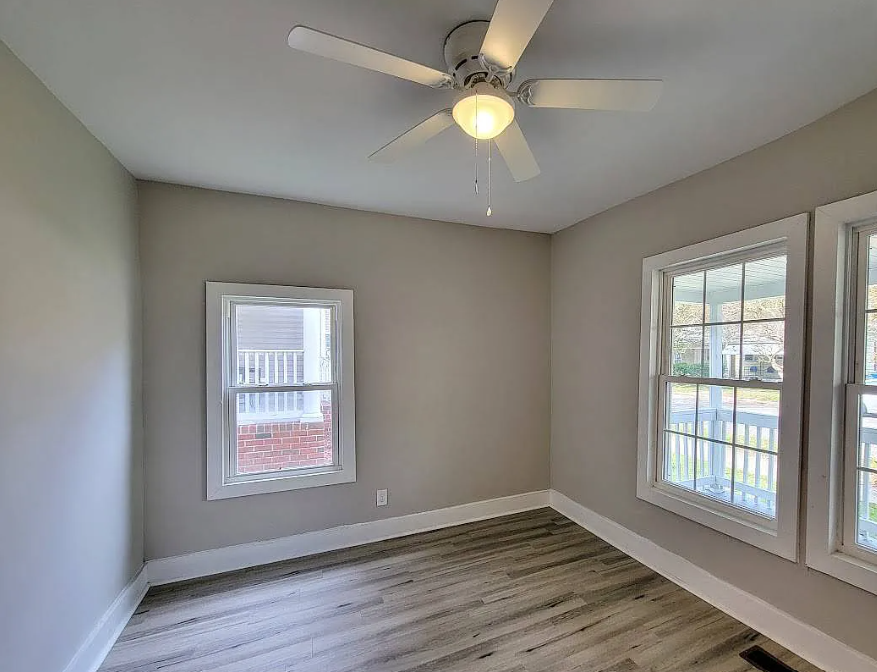 an empty living room with a ceiling fan and two windows