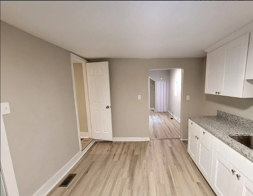 an empty kitchen with white cabinets and wood floors