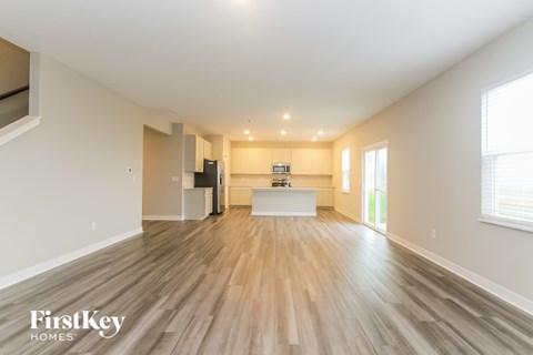 A spacious living room with wooden flooring and a kitchen area in the background.