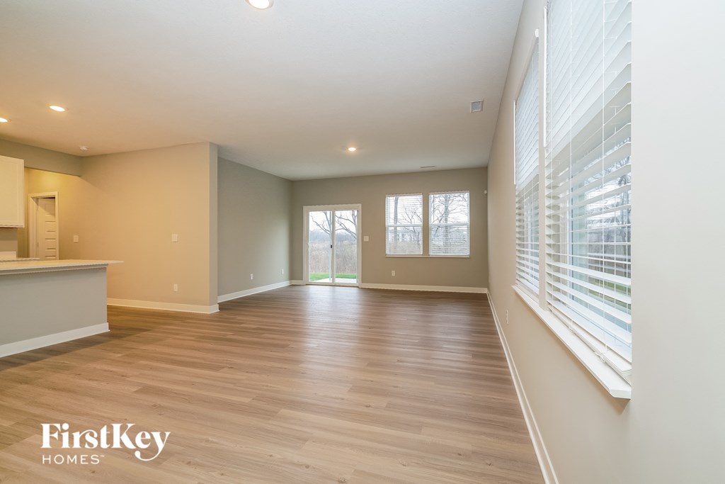 A spacious room with wooden flooring and a window with blinds.