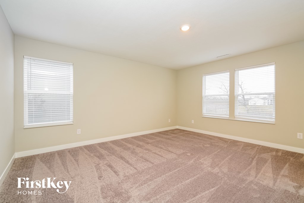 A room with a carpeted floor and two windows with blinds.