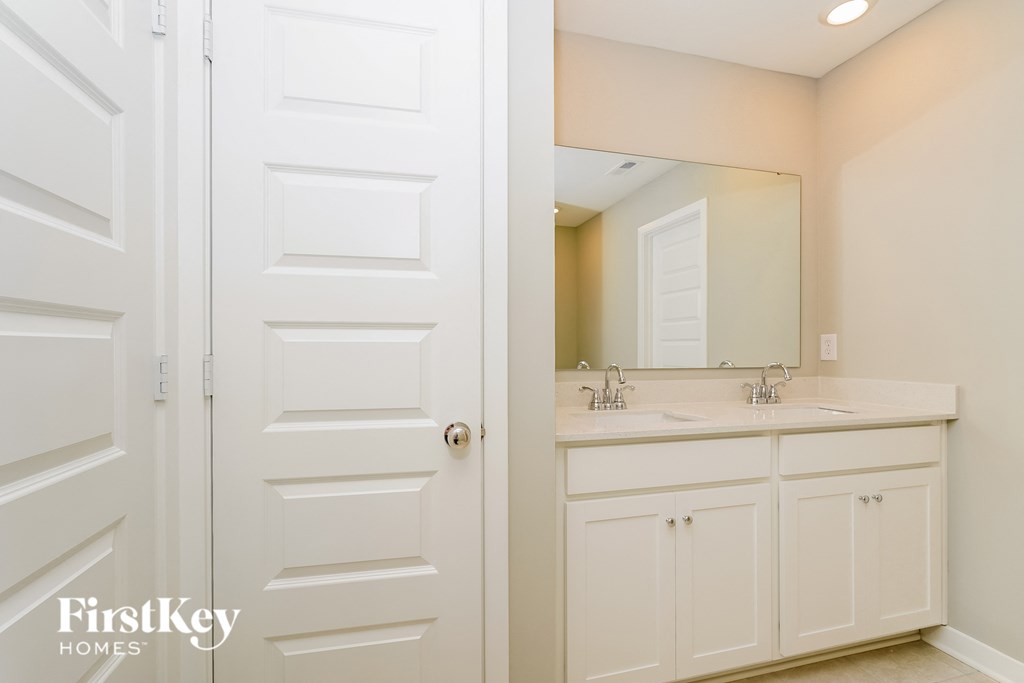 A white bathroom with a double sink and a mirror.