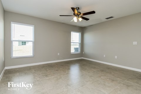 A spacious room with a ceiling fan and two windows.