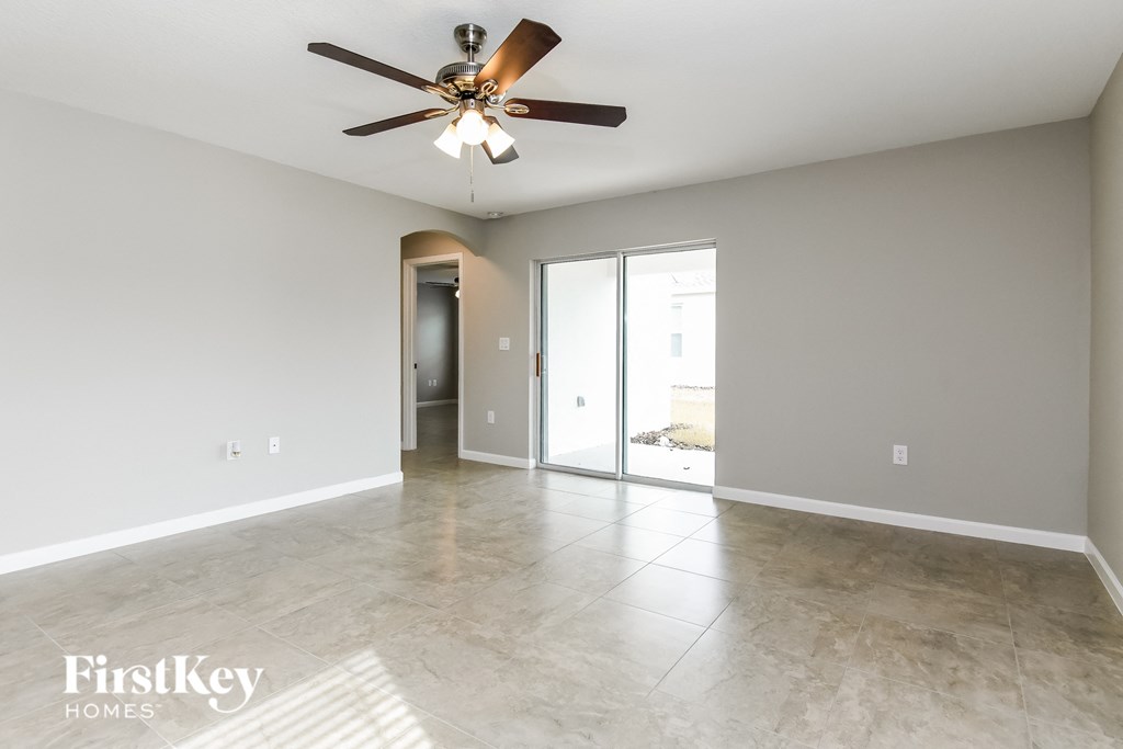 an empty living room with a ceiling fan and a door to a hallway