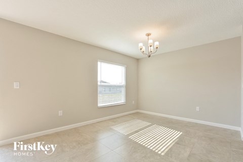 A room with a chandelier, a window with blinds, and a rug on the floor.
