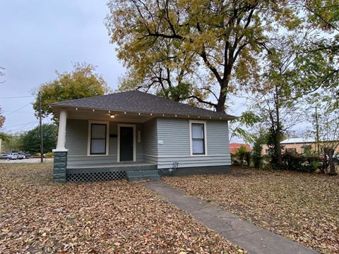 a small gray house with a sidewalk and trees