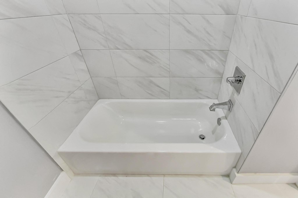 a white tile bathroom with a tub and a shower