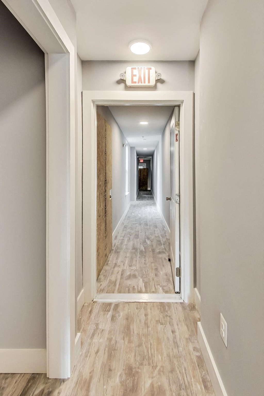 a hallway with an exit sign and a long hallway with wood floors