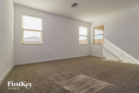a spacious living room with carpet and two windows