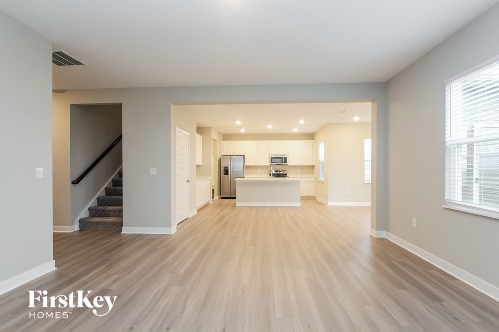 A spacious living room with wooden flooring and a staircase on the left side.