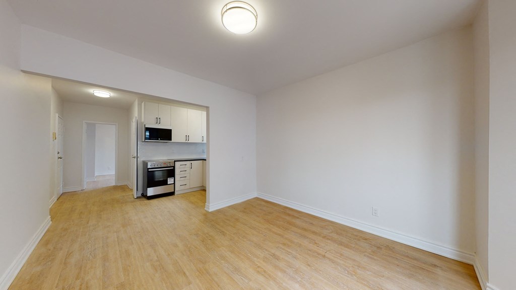 an empty living room and kitchen with white walls and wood flooring