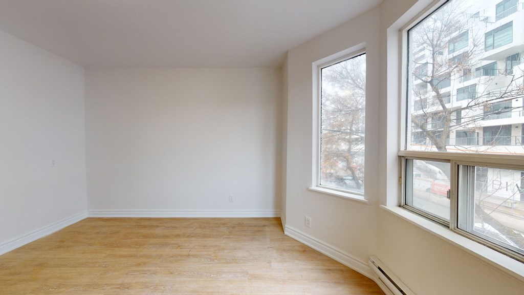 a bedroom with three large windows and wood flooring