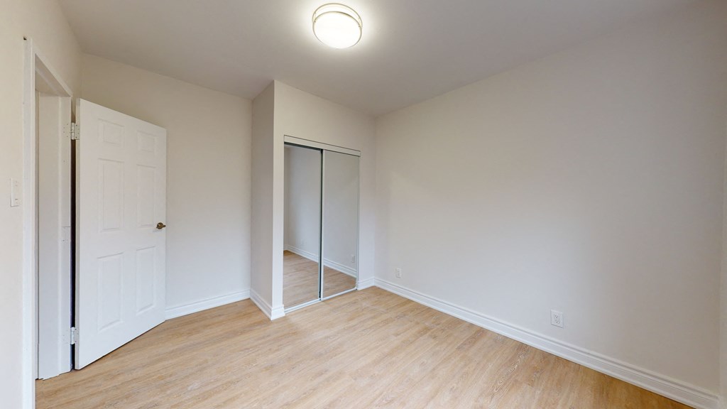 a bedroom with white walls and wood flooring and a mirrored closet