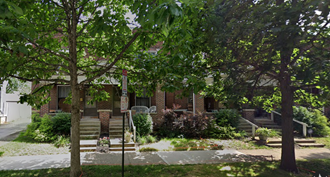 the front of a brick house with trees and a sidewalk